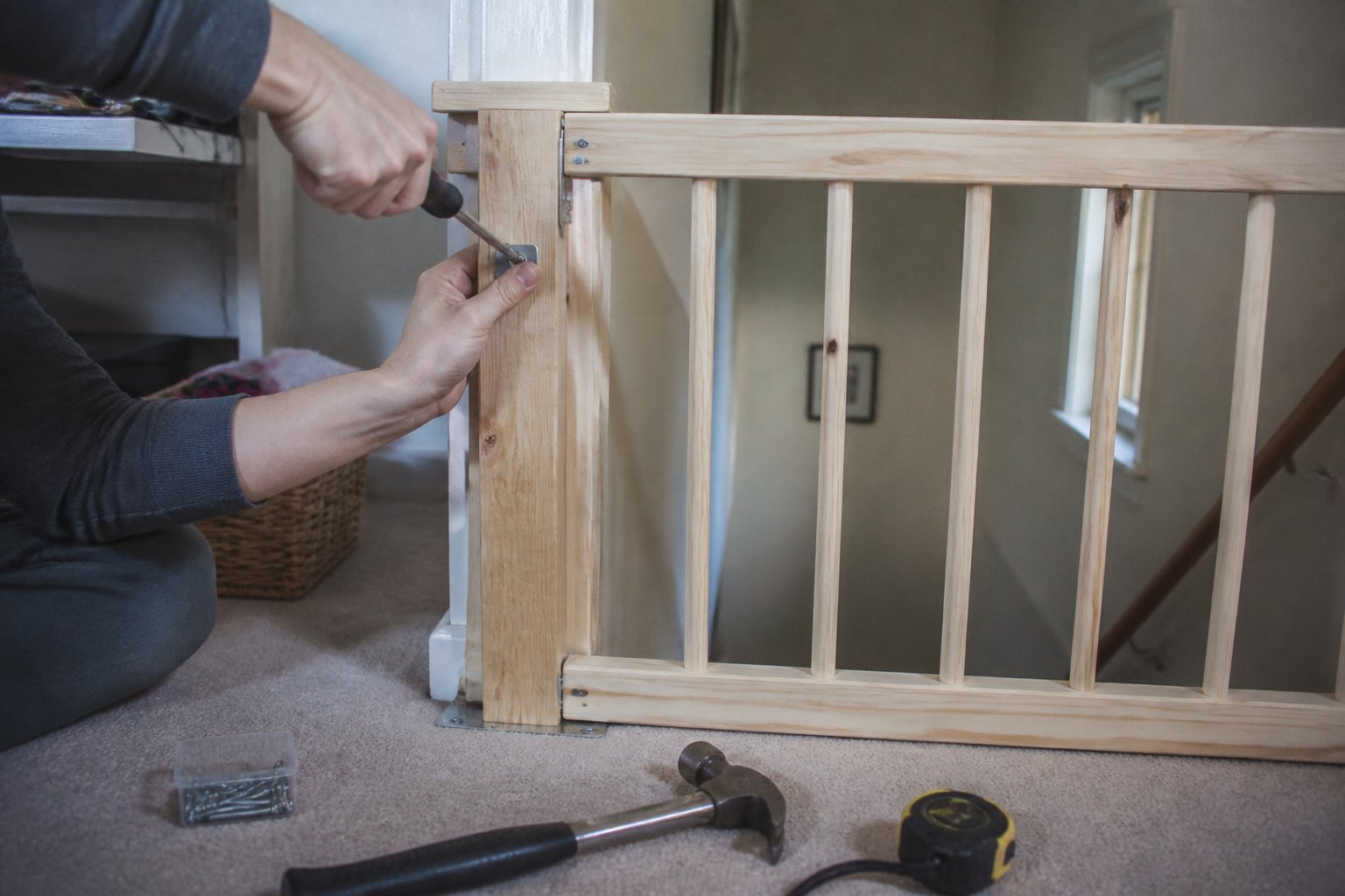 Hands assembling a simple wooden stairway gate on a home staircase with tools nearby.